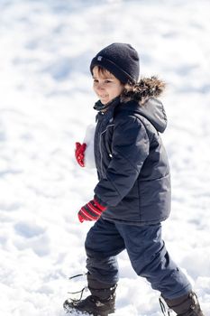 Cute boy playing with snow in the winter park in sunny day