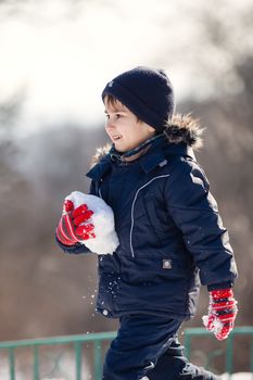 Cute boy in a winter jacket, playing with snow