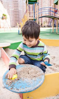 Cute boy playing in sandbox with a sand toys