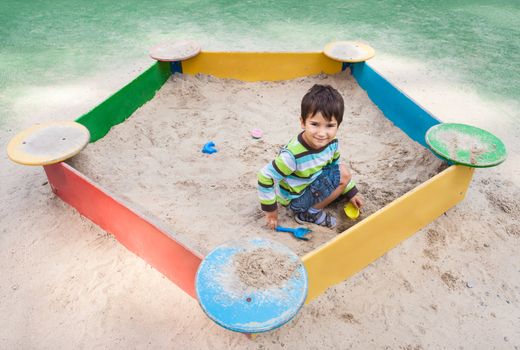 Cute boy playing in sandbox with a sand toys