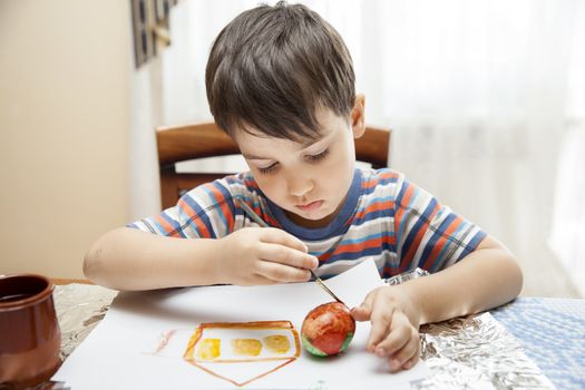 Home and family. Little boy draws house and easter egg with watercolor