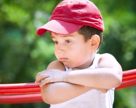 3-4 years old boy standing on a playground in a red cap on the blurred natural background