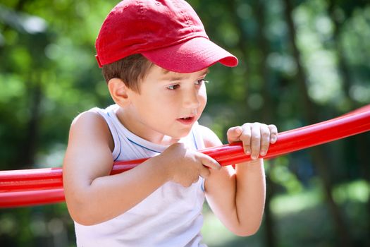 3-4 years old boy standing on a playground in a red cap on the blurred natural background