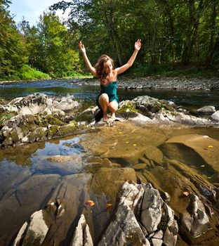 Young  woman with arms stretched out playing with water near the forest river