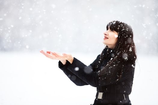 Happy beautiful young woman catches snowflakes