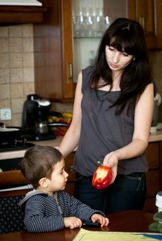 Mother offers red Bulgarian pepper to her child in kitchen