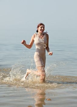 Woman in retro swimsuit smiles and runs through the water against the sea