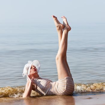Coquettish woman in retro swimsuit lying in the water at the beach feet up