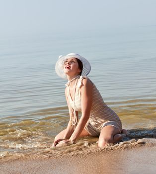 Woman in a striped retro bathing suit kneeling in the water at the beach