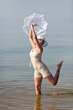 Woman in a striped retro bathing suit with a white parasol against the sea