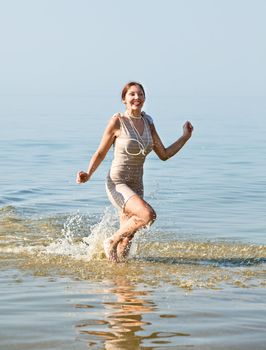 Woman in retro swimsuit smiles and runs through the water against the sea