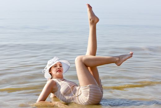 Woman in a striped retro bathing suit in the white hat posing against the sea