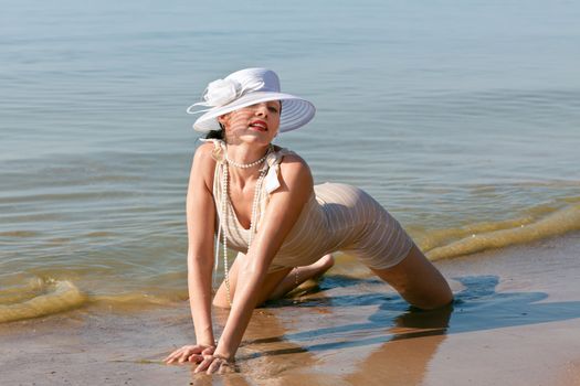 Woman in a striped retro bathing suit in the white hat posing against the sea