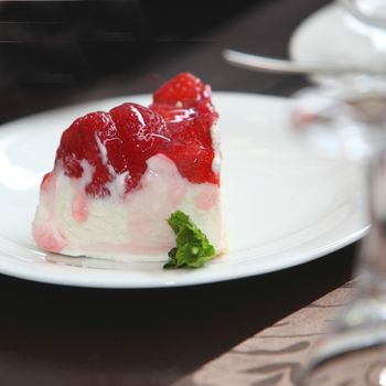 Delicious creamy cheesecake dessert topped with ripe red berries and served on a plate, closeup view with shallow dof