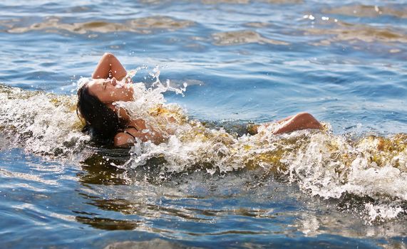 A young woman bathing in the sea wave with water splashes