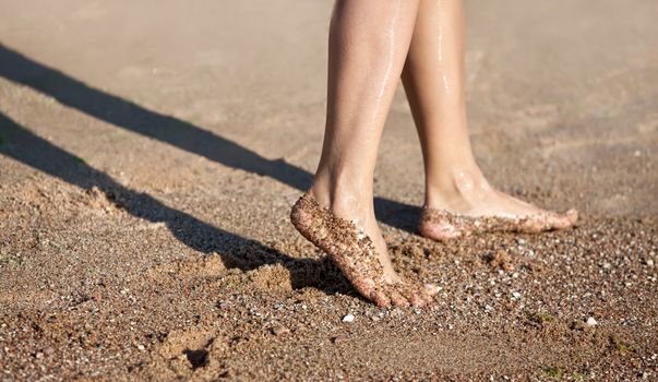 Girl's barefoot legs on the sand beach