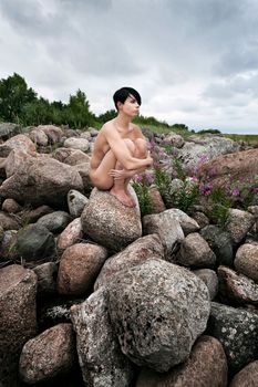 Beautiful nude woman sitting on stones against nature background