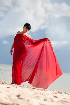 Young naked woman on a beach with red fabric
