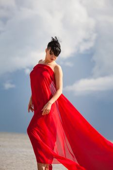 Young naked woman on a beach with red fabric