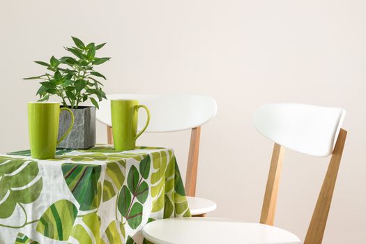 Two chairs and bright table with teacups and mint in a pot.