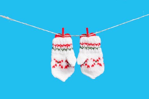 Two mittens and heart on clothesline with clothespins, isolated on blue background