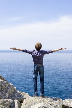 man on a mountain with open hands towards the word, blue sky end sea, freedom concept and travel