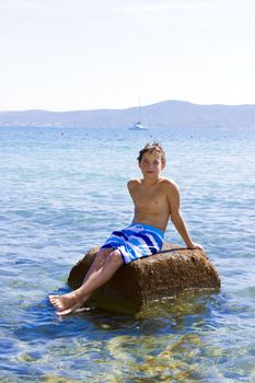 Cute eleven years old boy sitting on a rock in the sea