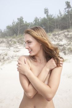Portrait of a young naked woman on a sandy beach on a foggy day