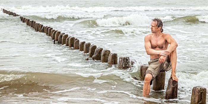 Middle-aged man sitting near the sea and looking thoughtfully into the distance