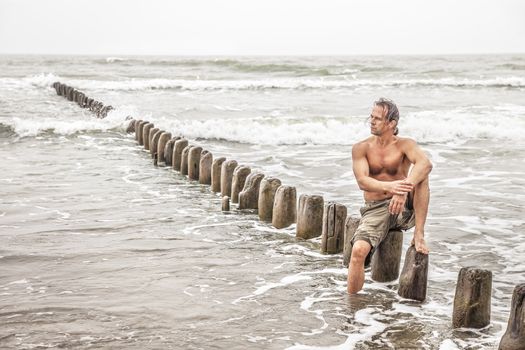 Middle-aged man sitting near the sea and looking thoughtfully into the distance