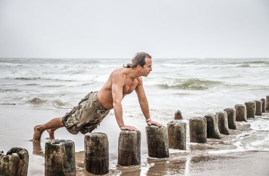 Middle-aged man doing pushups on the beach