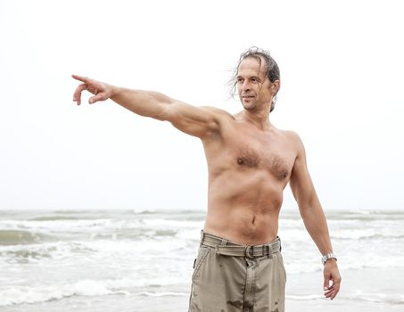 Middle-aged man enjoys nature by the sea and points to the something in the distance