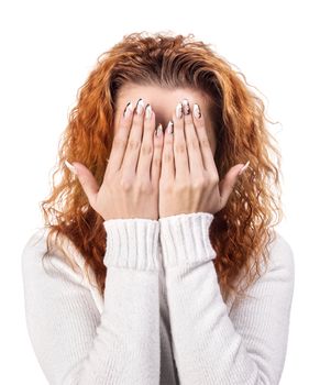 Portrait of red-haired woman covering her face by the hands, over white background