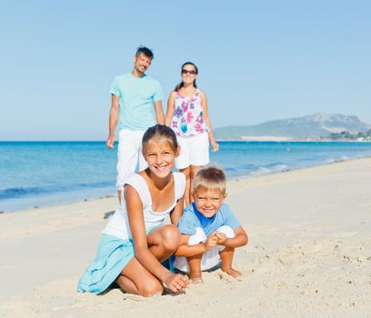 Two cute kids playing on tropical beach with their parents