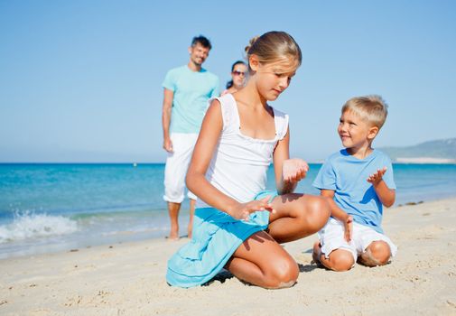 Two cute kids playing on tropical beach with their parents