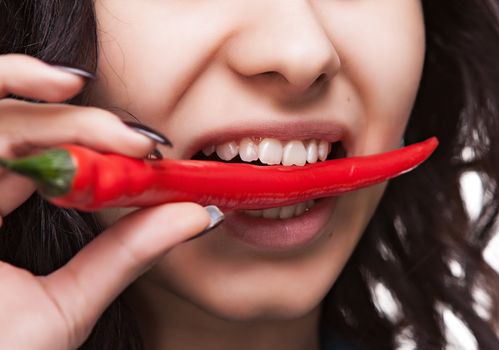 Young lady holding red hot chili pepper in mouth. Focus on lips