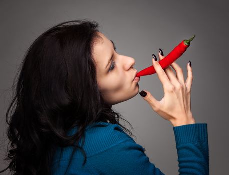 young lady holding red hot chili pepper in mouth