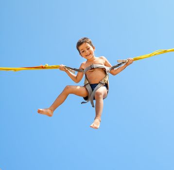 Little boy jumping on a trampoline on blue sky background 