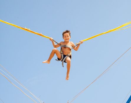 Little boy jumping on a trampoline on blue sky background 