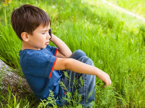 small boy in green grass talking on cell phone