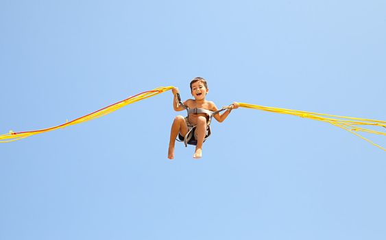 Little boy jumping on a trampoline on blue sky background 