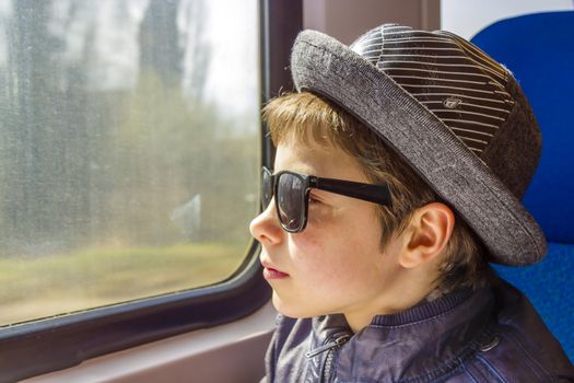 Handsome boy in sunglasses rides on a train