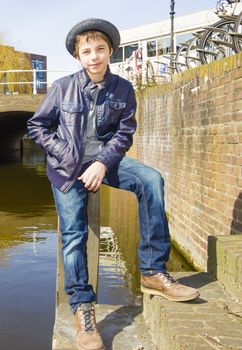 Cute teenage boy in hat (full-length portrait) against canal background
