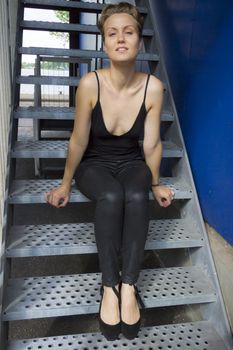 beautiful girl with blue eyes sitting on iron stairs against blue wall