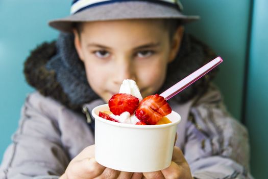 Cute teenage boy offering ice cream with strawberry and melon topping