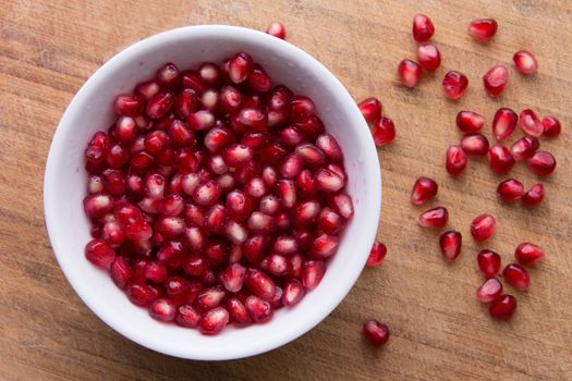 Pomegranate seeds are in a white bowl on the old cutting board