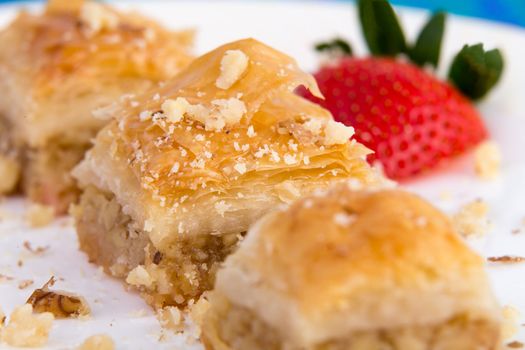 Three pieces of golden color baklava garnished with walnuts and strawberry, macro shot