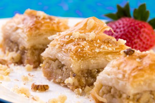 Three pieces of golden color baklava garnished with walnuts and strawberry, macro shot