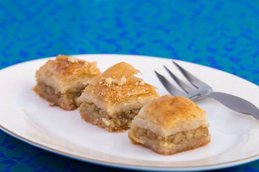 Three pieces of golden color baklava served on oval shape plate on green and blue color table cloth