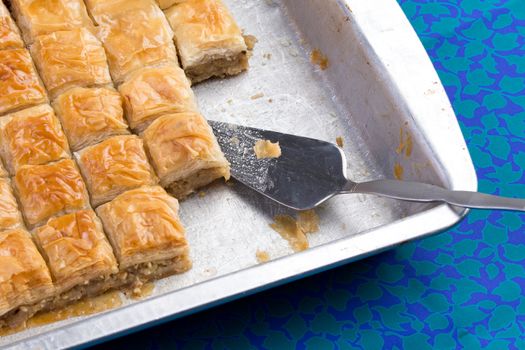 Home made baklava ready to serv from aluminum tray with brushed stailes-steel spatula